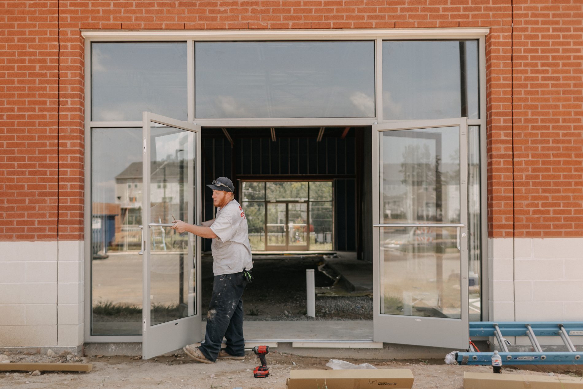 Installer fitting glass entry doors on a commercial storefront with a brick exterior