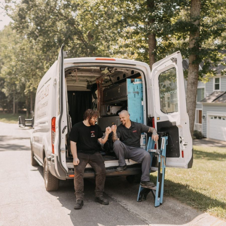 Two Budget Glass Company technicians sitting on the back of their work van